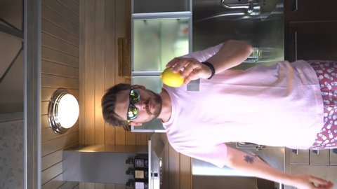 A young man in the kitchen participates in a challenge to eat a whole lemon, a freak eats a lemon on camera, vertical video for social networks, meme video.