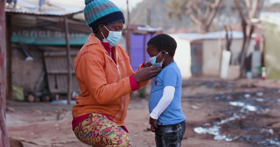 Poverty.Inequality.Black African mother puts a protective face mask on her young boy to prevent Covid-19 Coronavirus pandemic | Shutterstock HD Video #1056635741