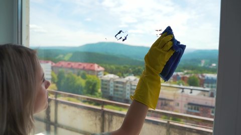 The young blond woman in the yellow gloves is washing a dirty window with a green sponge. woman working in a cleaning company cleans the glass.