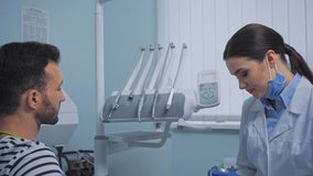 Patient looking at smiling dentist showing teeth model in clinic