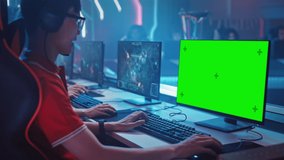 Professional Gamer Plays in a Video Game with Mock-up Green Screen Display on a Championship. Team of Pro Gamers in Stylish Neon Cyber Games Arena. Online Broadcasting of Tournament. Side View