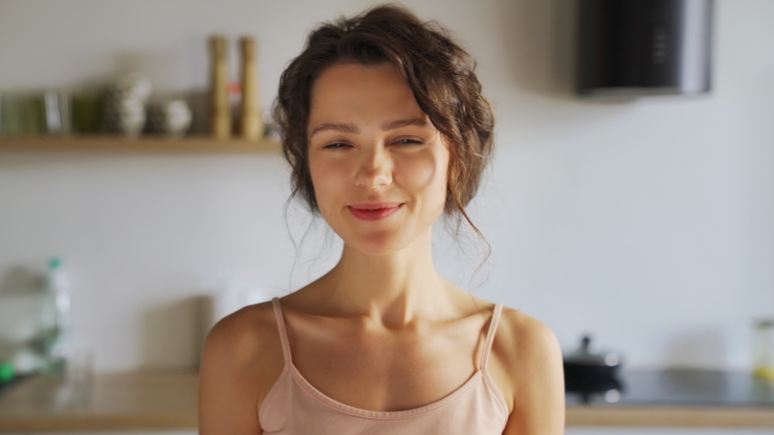 Young smiling beautiful woman pretty face looking at camera posing alone at home standing in kitchen. Girl with clean, healthy, glowing skin. Happy millennial caucasian girl close up front portrait  Royalty-Free Stock Footage #1056640646