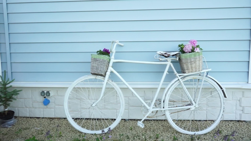 Retro Bicycle with two baskets of flowers on the background of a blue house. Garden decor in Provence style