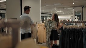 Caucasian woman in the store asks the guy's advice choosing between two dresses. The couple in love looking for clothes in store of modern clothing for shopping. Slow motion wide shot. - Powered by Shutterstock - Get 15% off with code: PIKWIZARD15