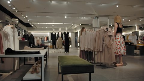 Time-lapse of empty clothes store with two women customers choosing clothes. Camera dolly movement. Fashionable retail with small amount of clients. Fast motion.