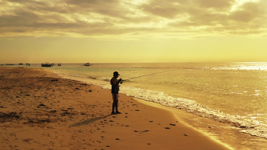 A man relaxing and fishing on the shoreline in the exotic holiday location of Antigua in the late afternoon during a stunning golden sunset
