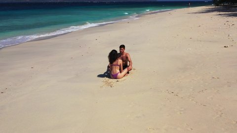 A young happy couple sitting on the warm sand of an Australian beach, bathing in the sunlight
