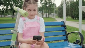 A girl sits on a bench with a phone and communicates on social networks.