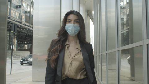 Young adult business woman commuting in city wearing protective face mask during pandemic on street