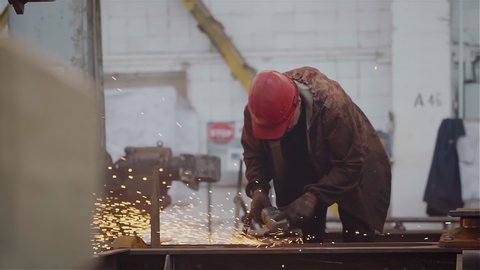 Factory Worker Grinds Metal Construction using angle grinder. Bright Golden Sparks comes out, Heavy Manual Work at Modern Steel Making Industry. Slow Motion. 