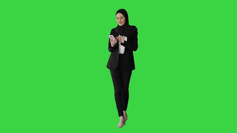Smiling Arab woman in hijab taking selfies on her mobile phone as she walks on a Green Screen, Chroma Key.