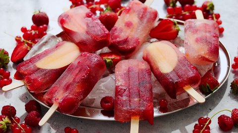Strawberry raspberry apple and red currant ice cream popsicles in metal tray with ice cubes. Placed on stone backdrop. Flat lay, top view.
