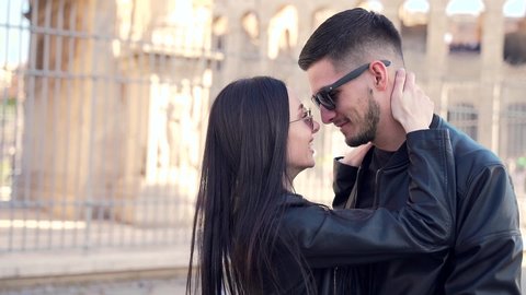 Portrait couple of young people in love in black clothes. leather jacket and sunglasses. Against the background Colosseum and the arch. Man and woman tourists hugging holding hands and dancing. 
