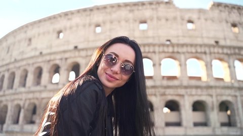 Portrait of a young young woman on a background of the Colosseum. Stylish attractive female in sunglasses posing for the camera. Woman tourist on the background of the amphitheater of Rome, Italy.