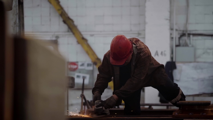 Welder in Red Helmet and Protective Glasses Works Manually with angle grinder, Shaping Metal Construction, Sparks at industrial production line at modern factory | Shutterstock HD Video #1056647402