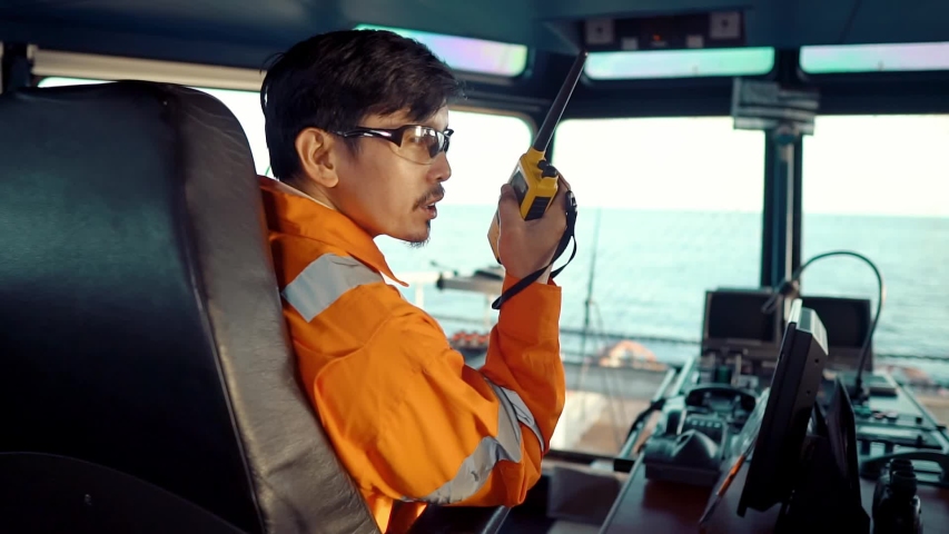Filipino deck Officer on bridge of vessel or ship wearing coverall during navigaton watch at sea . He is speaking on GMDSS VHF radio, communication between vessels. | Shutterstock HD Video #1056648782