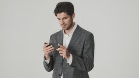 Happy cheerful handsome business man isolated over white wall background while using mobile phone and watching videos