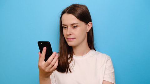 Young woman hold modern phone laughing over prank online funny video, enjoy distant chat, isolated on blue background. Free time and have fun use internet amusements modern gadgets usage concept