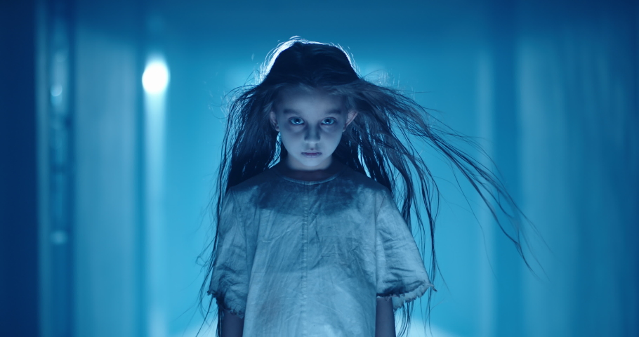 Little caucasian girl in ghost white sundress costume for halloween party creepily staring at camera while mistique wind blows her hair 4k footage | Shutterstock HD Video #1056653246