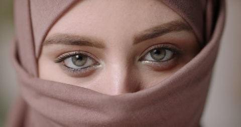 Face with natural make up of attractive muslim gir wearing traditional hijab scarf. Her brown and green eyes looking at camera - beauty, islam concept extreme close up 4k footage