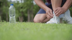 Asian man tying shoes lace while jogging exercise at the park on green grass, outdoor exercising, active lifestyle, stay hydrated water bottle placing on the side, runner grab water bottle and go - Powered by Shutterstock - Get 15% off with code: PIKWIZARD15