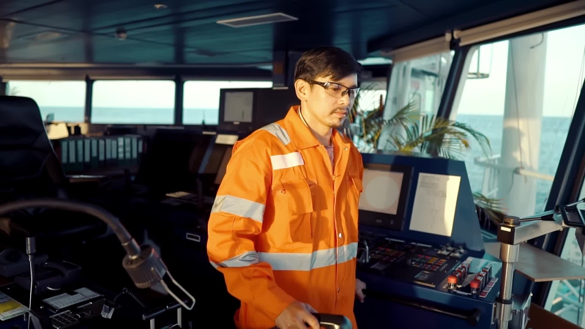 Filipino deck Officer on bridge of vessel or ship wearing coverall during navigaton watch at sea . He is speaking on GMDSS VHF radio, communication between vessels.