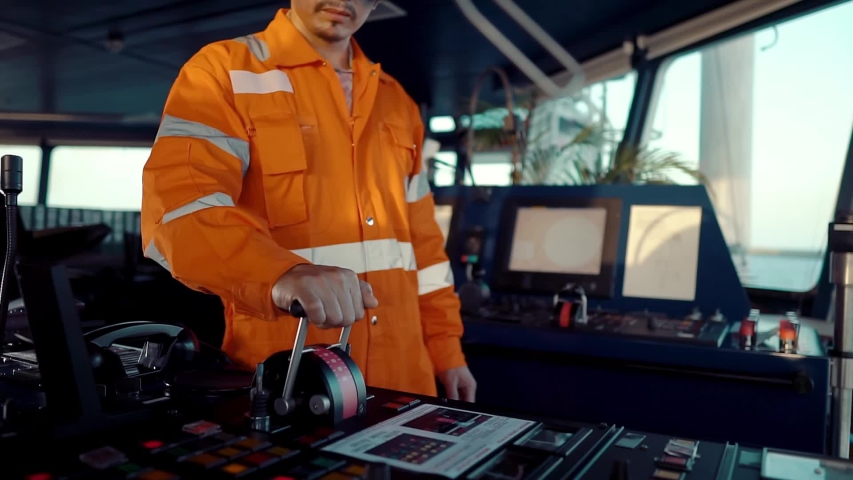 Filipino deck Officer on bridge of vessel or ship wearing coverall during navigaton watch at sea . He is maneuvering with cpp thrusters propulsion