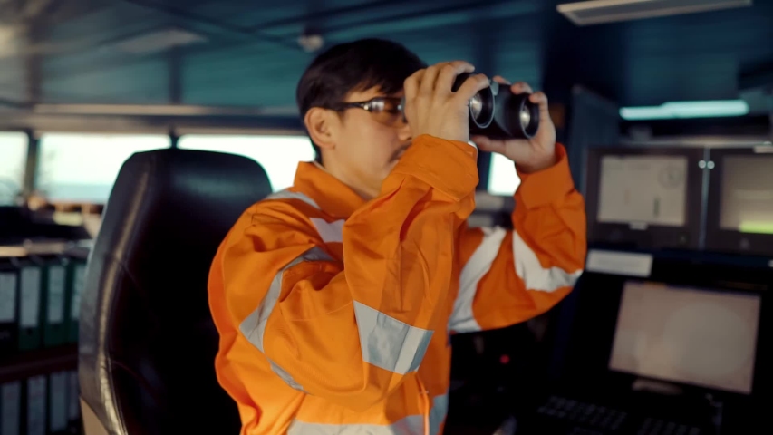 Filipino deck Officer on bridge of vessel or ship wearing coverall. He is looking through binoculars. COLREG navigaton watch at sea