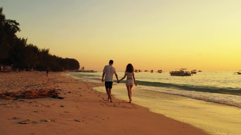Beautiful young couple in love walking along the beach while the waves flood the beach enjoying the sunset