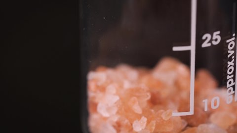 Orange pink crystals dropped into glass beaker, closeup detail with black background Video stock
