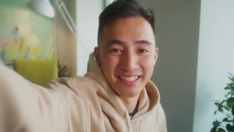 smart Asian guy using pov video call communicate with business colleague friend from home during self isolation from coronavirus outbreak crisis. A man wearing headphone looking camera.
