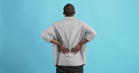 Black man holding his hands behind his back, stretching spine, blue studio background, side view
