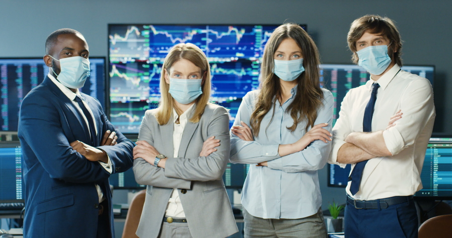 Portrait of young male and female mixed-races traders in medical masks in stock exchange office. Multiehnic men and women investors posing and looking at camera in trading room. Teamwork concept. Royalty-Free Stock Footage #1056665333
