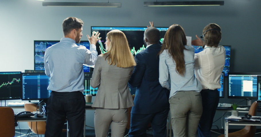 Rear of male and female multiethnic brokers standing in office with monitors, turning to camera and celebrating success. Cheerful happy businessmen and businesswomen dancing and laughing after trading Royalty-Free Stock Footage #1056665342