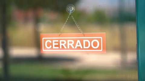 Open and close sign in spanish changed by a hand inside a glass door