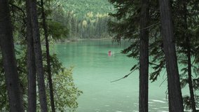4K video of two people in red canoe on beautiful forest lake while they enjoy summer paddling on the calm green water
