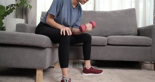 Sporty young asian woman doing exercising with dumbbells and watching fitness video tutorial online on laptop in the living room, Sport at home training, online fitness class, Healthy lifestyle.