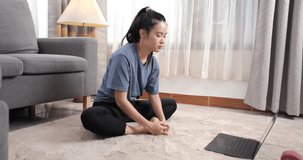 Sporty young asian woman in t-shirt doing stretching and watching fitness video tutorial online on laptop with dumbbells in the living room, Sport at home training, online fitness class concept.