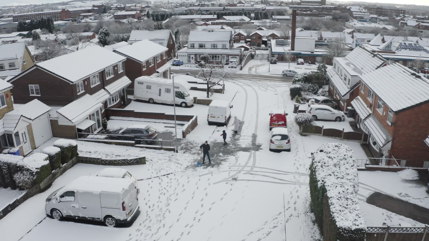 A family scrape snow and ice from their driveway and the road after a heavy snowfall, blizzard in the West Midlands, Longton, Stoke on Trent, Staffordshire