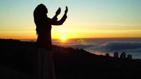 Eid al-Adha Islamic holiday. Silhouette of Muslim woman making Dua to Allah outdoor. Beautiful dawn, sunrise