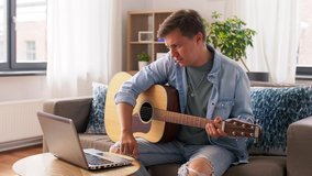 leisure, music and people concept - young man with laptop computer having video call and playing guitar at home