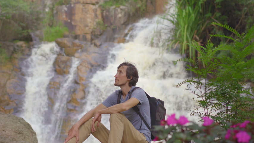 A young man tourist visits waterfall in mountains. Travel to Dalat concept