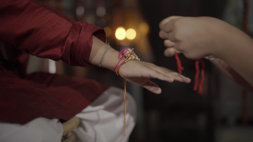 Closeup of hands, sister tying rakhi, Raksha bandhan to brother's wrist during festival or ceremony - Raksha Bandhan celebrated across India as selfless love or relationship between brother and sister | Shutterstock HD Video #1056675851