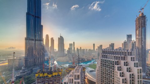 Panoramic skyline view of Dubai downtown during sunrise with mall, fountains and tallest tower aerial morning timelapse. Modern skyscrapers and cloudy sky with sun rays
