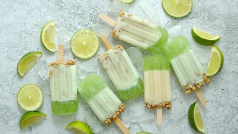 Lime and cream homemade popsicles or ice creams placed with ice cubes on gray stone backdrop. Flat lay, top view.