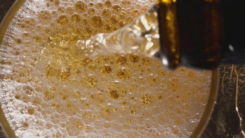 Pouring beer into a glass. View from above. A jet of beer is poured into the glass, covering the bottom with foam and raising the level to the top of the glass.
