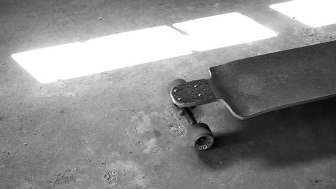 Shot in black and white, a longboard skateboard is pushed through screen on a cement background.