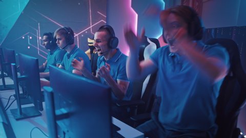 Diverse Esport Team of Pro Gamers Play in Computer Video Game and Win Championship, Celebrate with High-Fives. Neon Cyber Games Arena. Online Streaming of Tournament. Side Gliding Dolly View