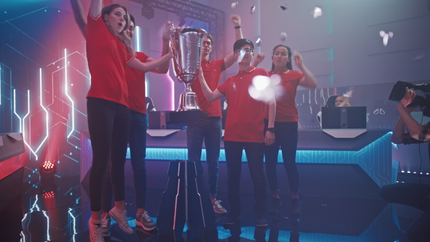 Diverse Esport Team Winner of the Video Games Tournament Celebrates Victory Cheering and Lifting Trophy in Big Championship Arena. Cyber Gaming Event with Gamers and Fans. Elevating Slow Motion Shot Royalty-Free Stock Footage #1056687344