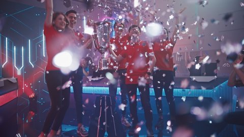Diverse Esport Team Winner of the Video Games Tournament Celebrates Victory Cheering and Lifting Trophy in Big Championship Arena. Cyber Gaming Event with Gamers and Fans. Elevating Slow Motion Shot